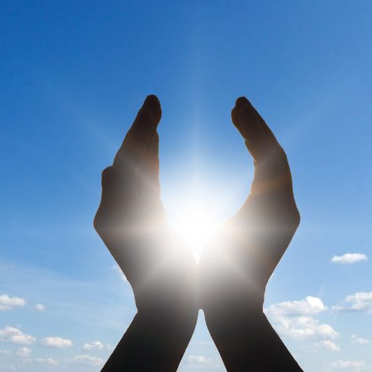2 hands raised against sky with energy between them